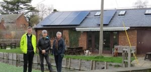 South Oxfordshire District Councillors Robin Bennett, Andrea Powell and Sam Casey-Rerhaye at Ewelme Watercress Beds. Behind them, a red-brick building has 10 new solar panels on its roof.