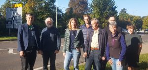 A group of councillors and residents stand on the verge by the side of a road.